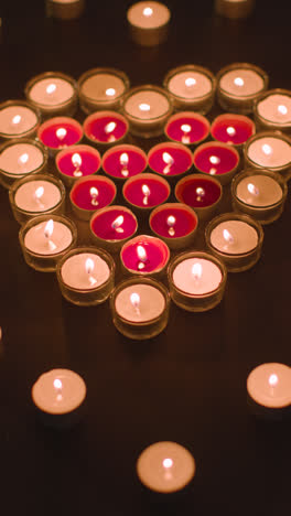 Vertical-Video-Of-Romantic-Red-And-White-Candles-In-the-Shape-Of-A-Heart-On-Black-Background